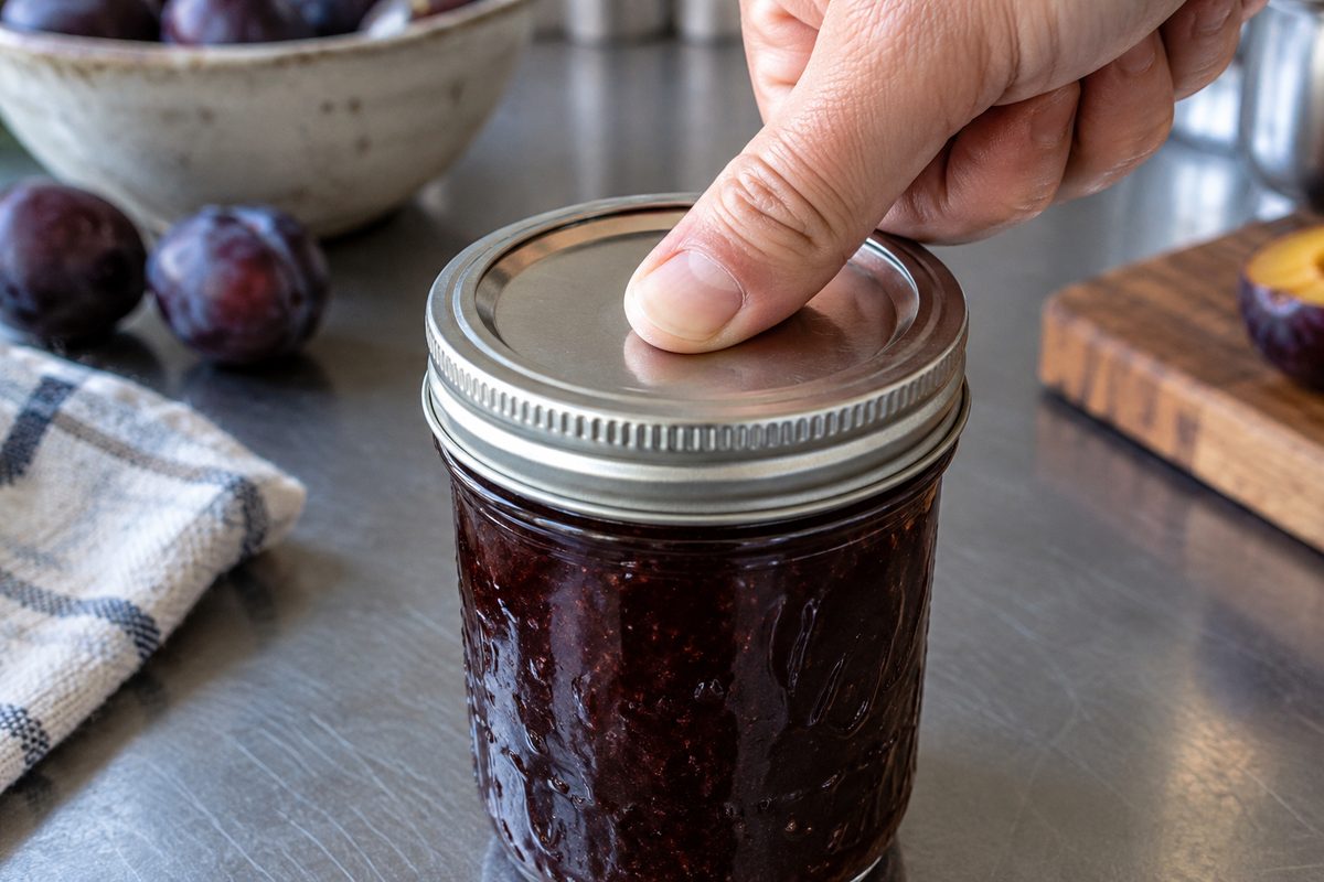 A thumb pressing a jar lid to check the seal has held